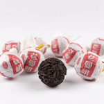 A group of My Store Ripened Dragon Pu'er Tea Pearls, wrapped in red and white paper, surrounds a single unwrapped dark tea ball, highlighting the rich Yunnan Pu'er on a white background.