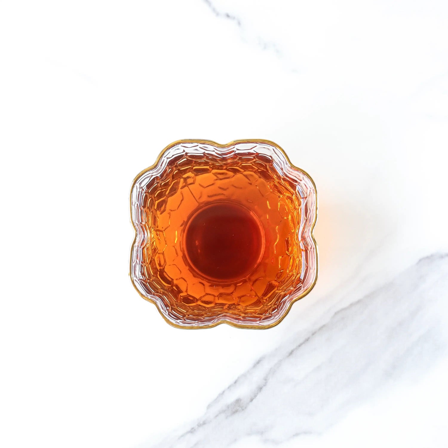 A top-down view of a glass with amber liquid, likely brewed from My Store's Ripened Dragon Pu'er Tea Pearls, set on a white marble surface.