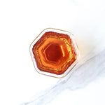 A top-down view of a glass filled with amber-colored Small Ripened Pu'er Tea Cakes by My Store, set on a white marble surface.