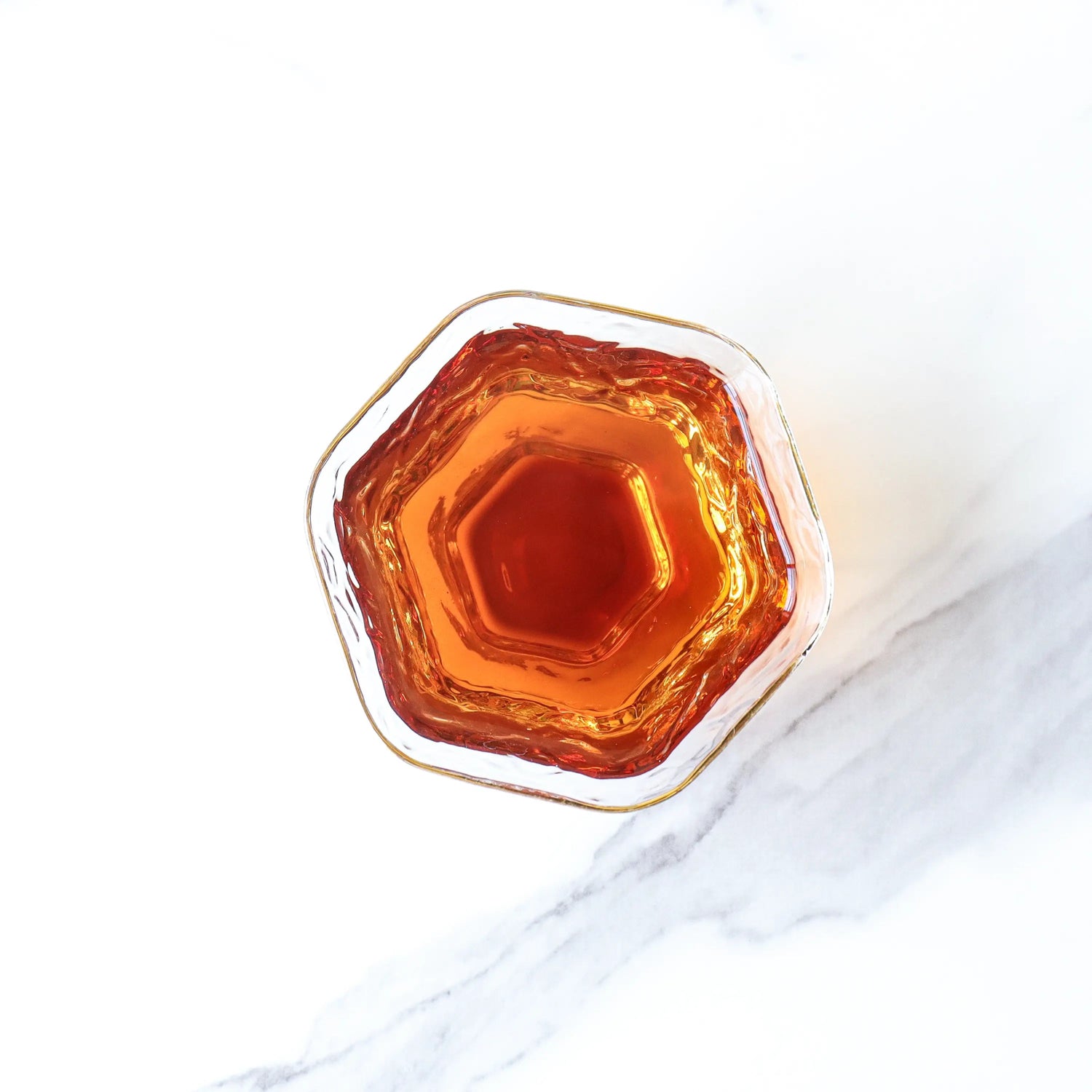 A top-down view of a glass filled with amber-colored Small Ripened Pu'er Tea Cakes by My Store, set on a white marble surface.