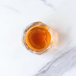A clear glass cup of Ripened Pu'er Tea from My Store, viewed from above on white marble, reveals the amber hue formed by its signature fermentation process.