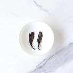 Two Ripened Pu'er Tea leaves from My Store rest side by side in a small white bowl on a white marble surface.