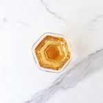 A hexagonal glass filled with My Store’s Dianhong Rose Black Tea sits on a white marble surface, its amber hue reminiscent of Yunnan rose petals.