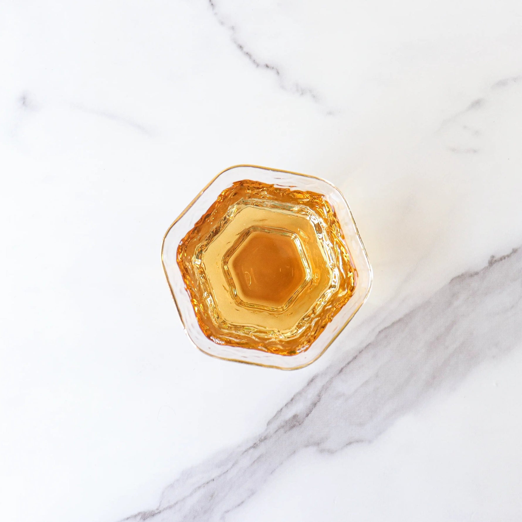 A hexagonal glass filled with My Store’s Dianhong Rose Black Tea sits on a white marble surface, its amber hue reminiscent of Yunnan rose petals.