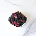 A small white bowl of My Store's Dianhong Rose Black Tea, featuring black tea and dried rose petals, sits on a white marble surface.