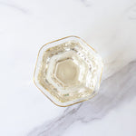A hexagonal glass with a gold rim, filled with My Store’s Silver Needle White Tea—rich in antioxidants—is photographed from above on a white marble surface.