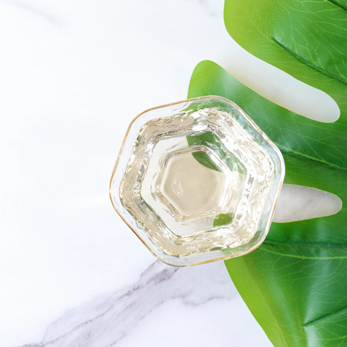 Brewed Silver Needle White Tea in a hexagonal glass beside a green leaf.