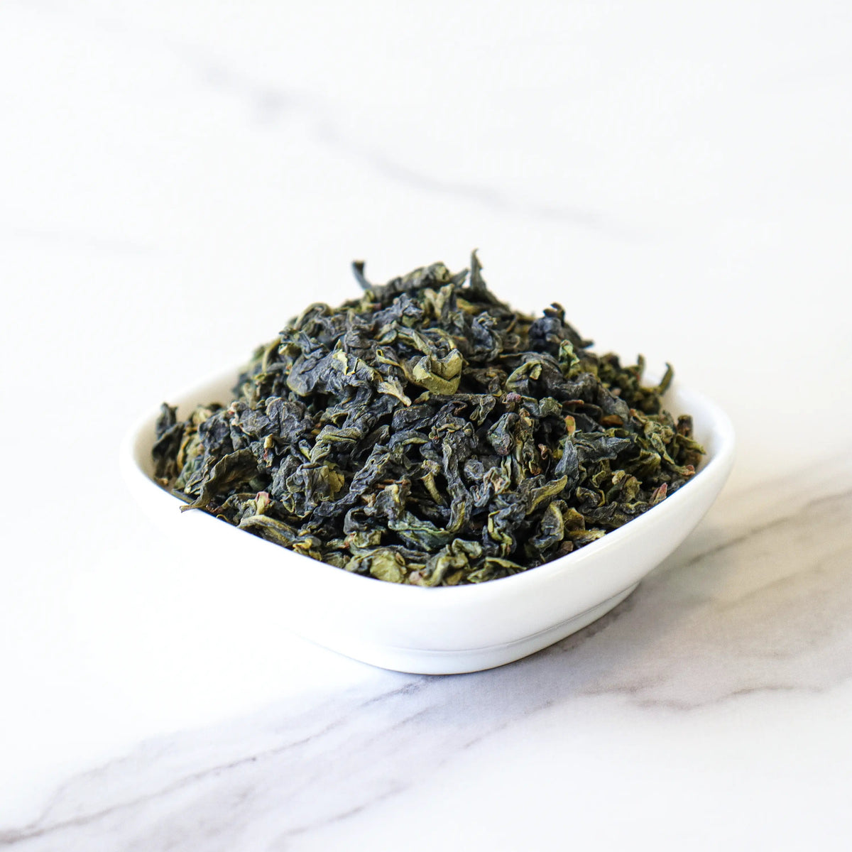 Loose Tie Guan Yin Oolong Tea leaves in a white bowl on a marble surface.