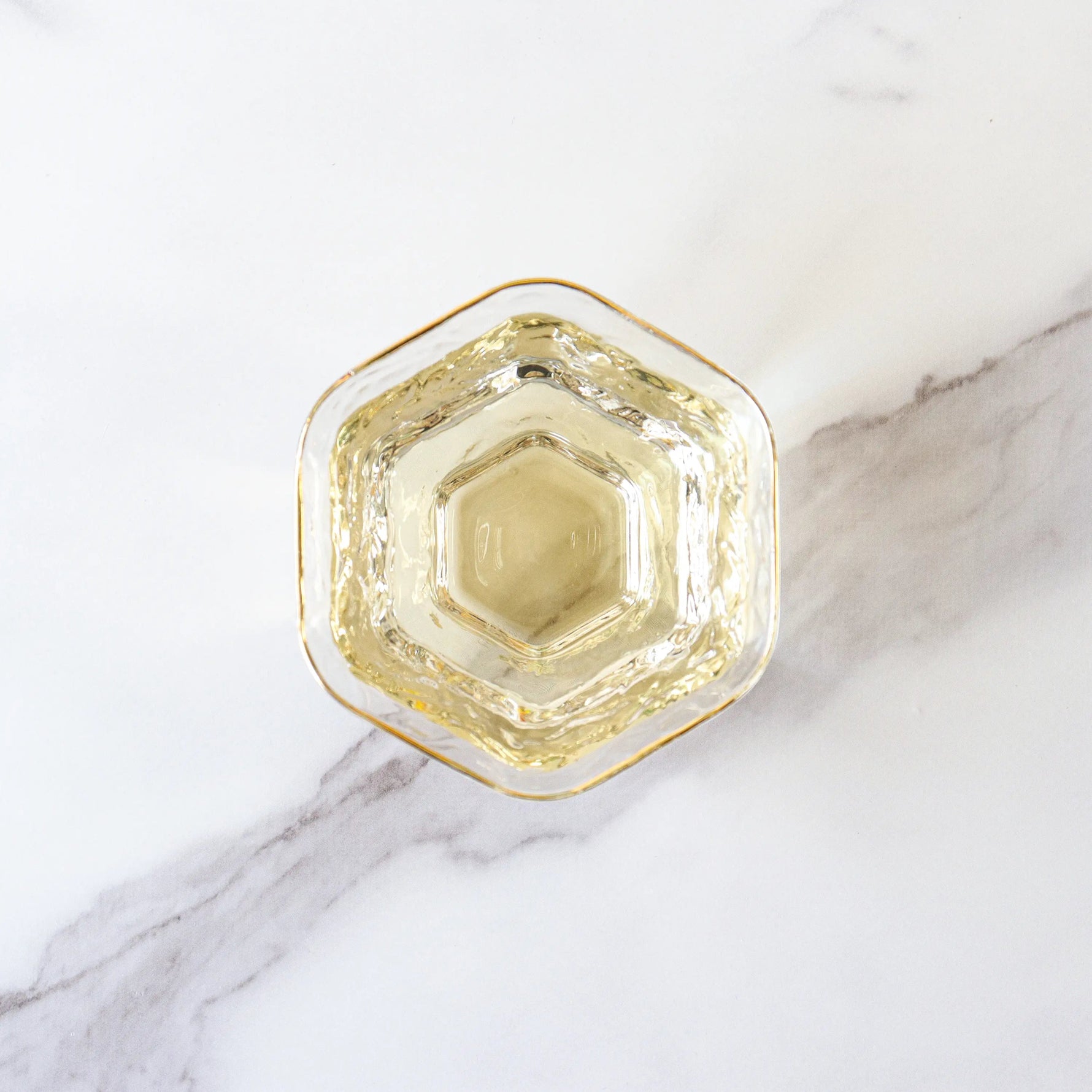 A hexagonal glass filled with My Store's Tie Guan Yin Oolong Tea, famous for its orchid aroma and light color, is placed on a white marble surface.