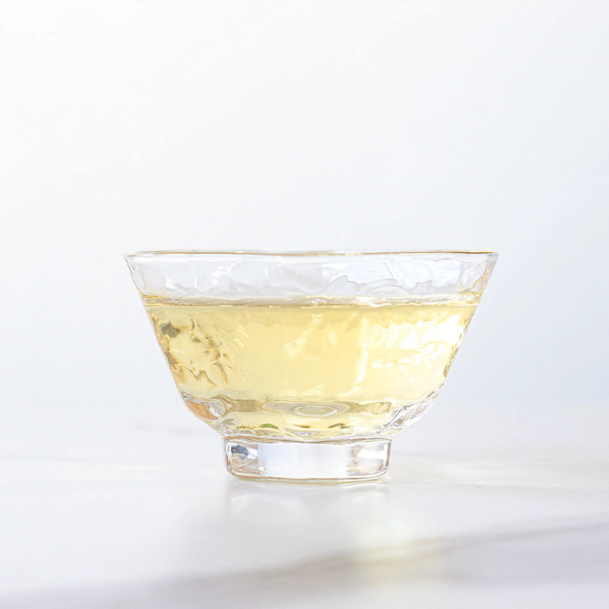 Brewed Tie Guan Yin Oolong Tea in a clear glass cup on a white surface.