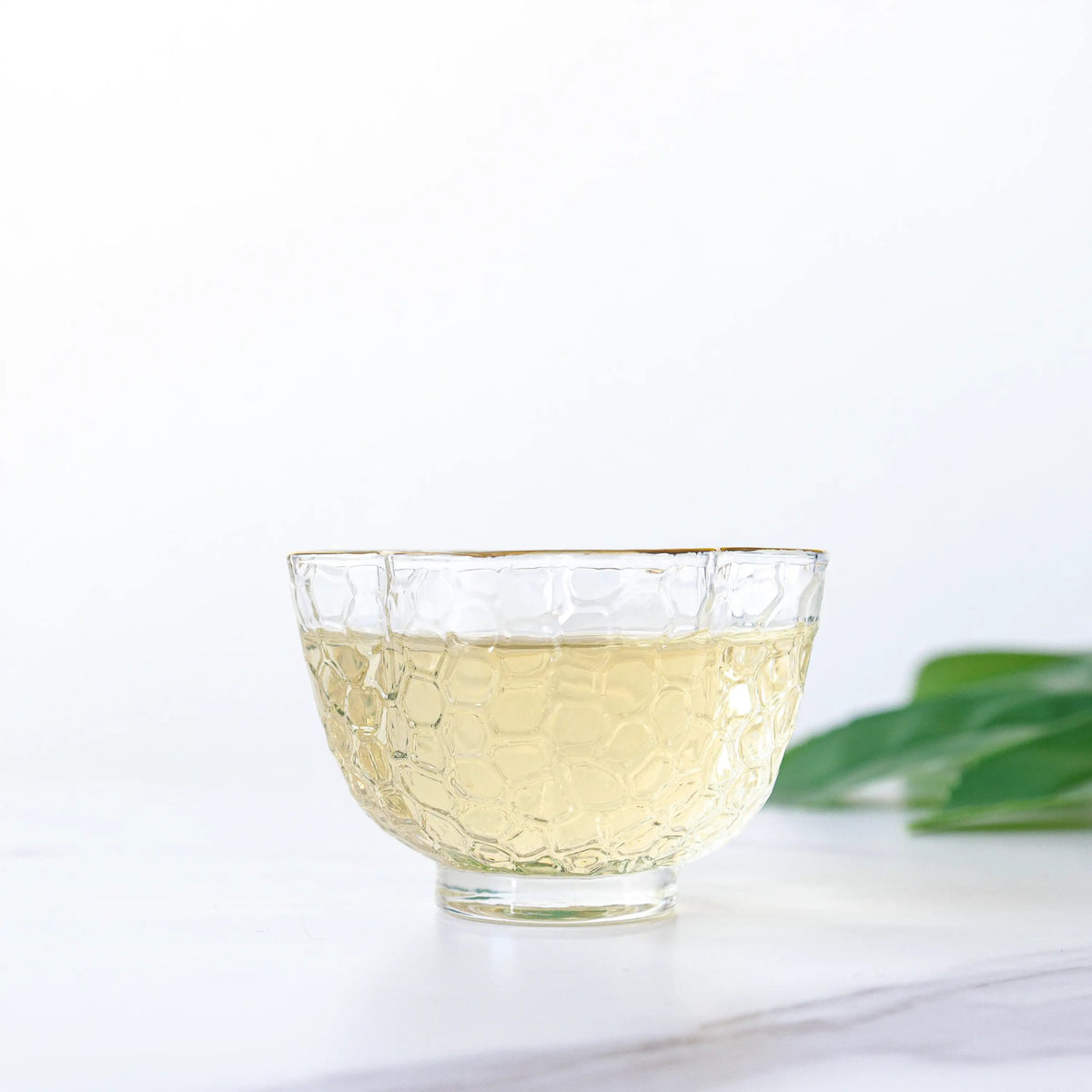 Pale White Peony tea in a clear glass cup on a white surface.
