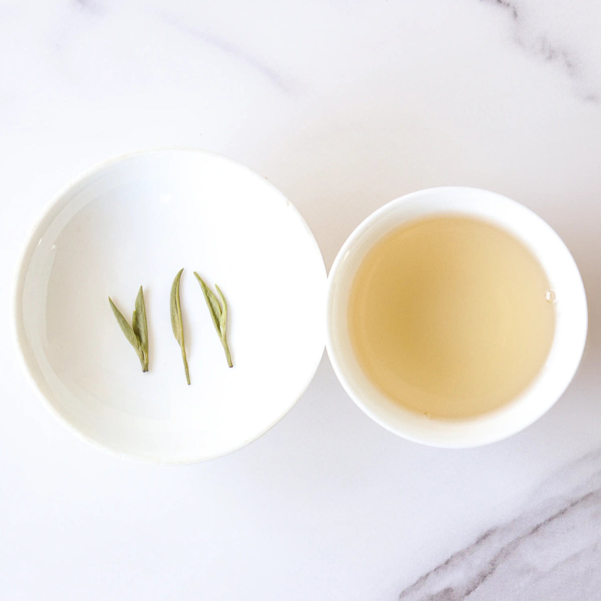 Xinyang Maojian Green Tea liquor beside three leaves on a small white plate