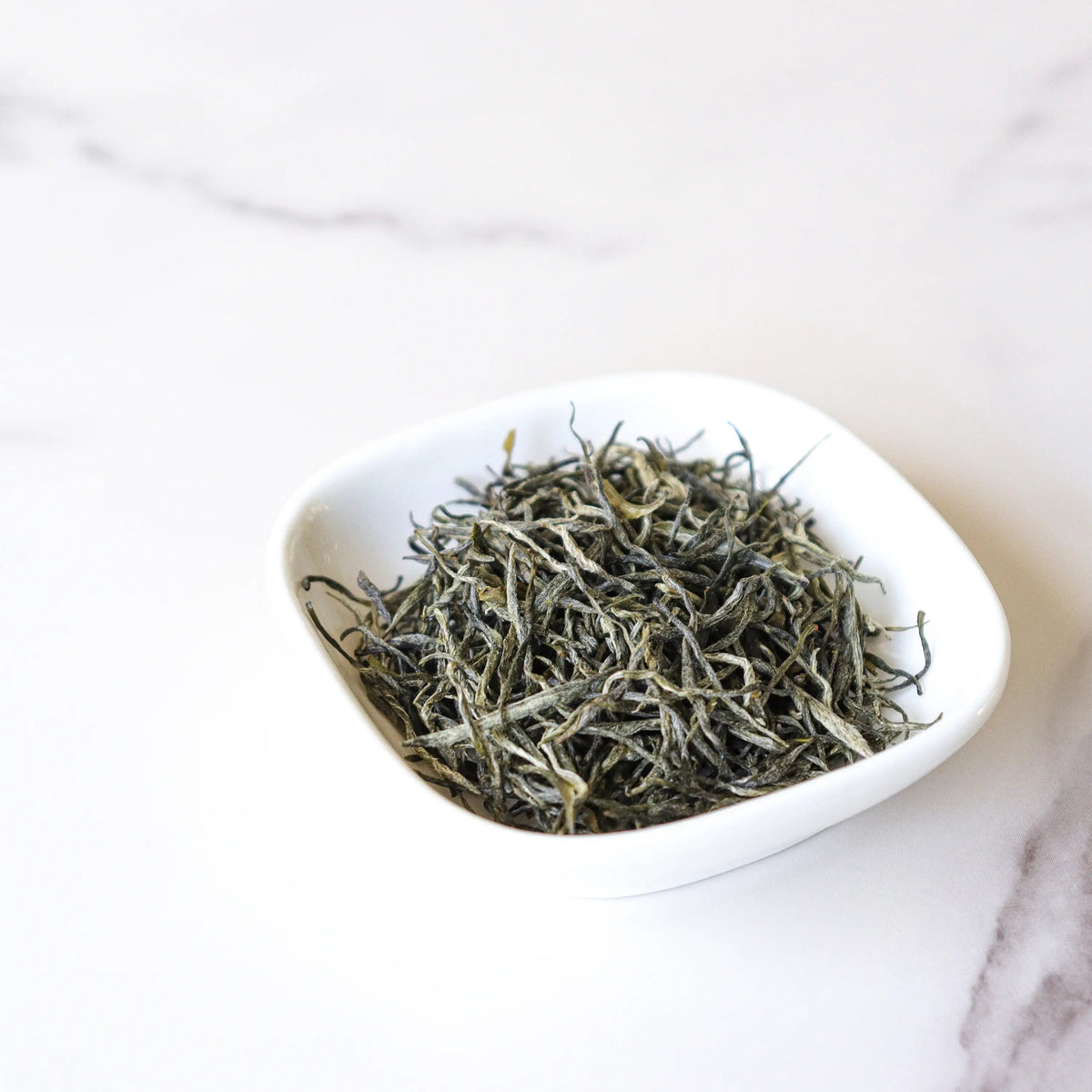 Xinyang Maojian Green Tea loose leaves in a small white bowl