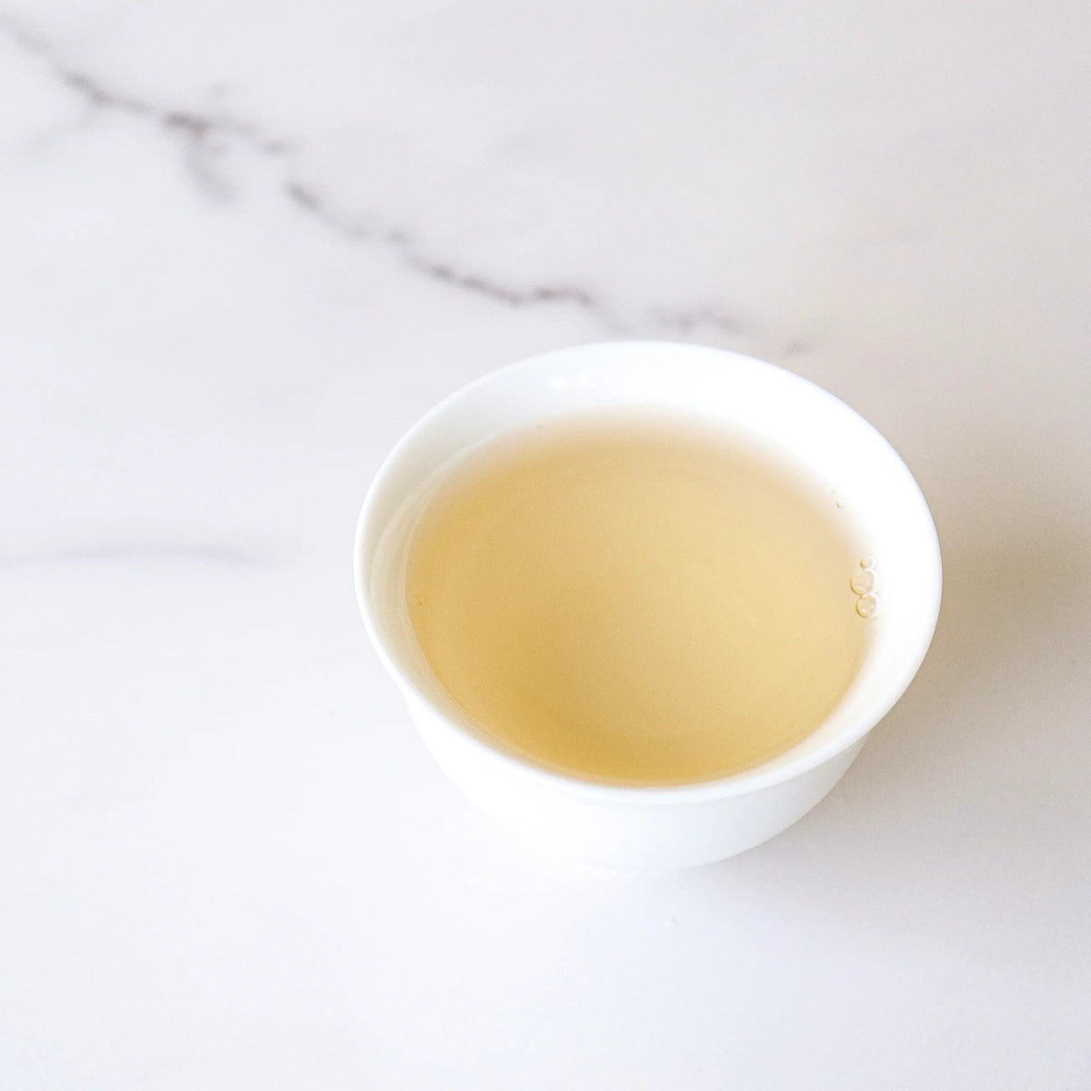 Light yellow Xinyang Maojian Green Tea liquor in a white cup on marble