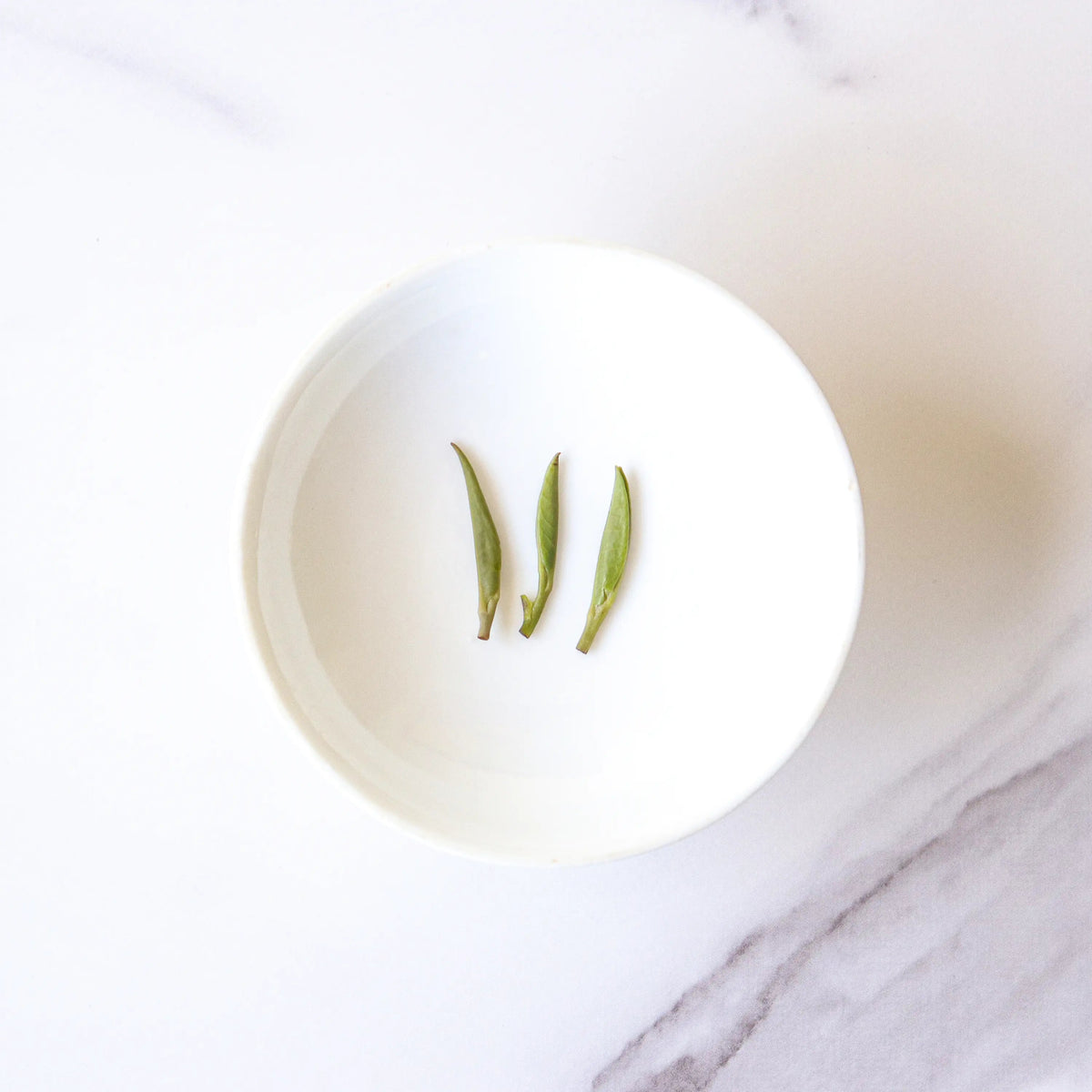 Three Zhu Ye Qing Green Tea leaves on a small white plate